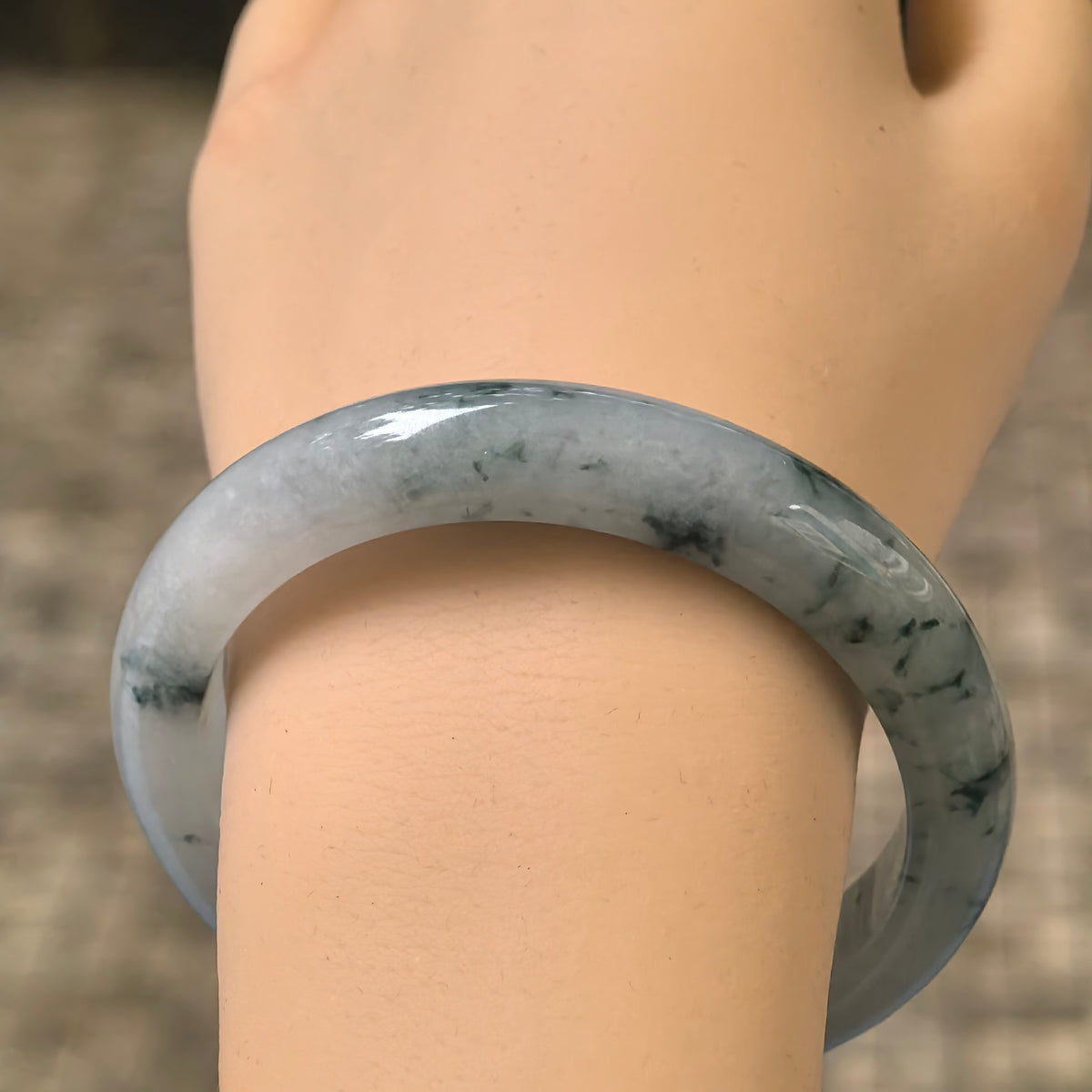 Front wrist view of the pale green jadeite bangle, highlighting its polished surface and delicate dark green floating patterns.