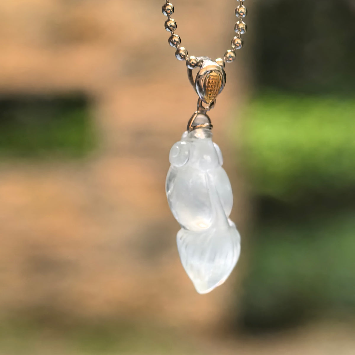 Icy white jadeite goldfish pendant suspended from a chain, showing its translucent body and 18K gold bail.