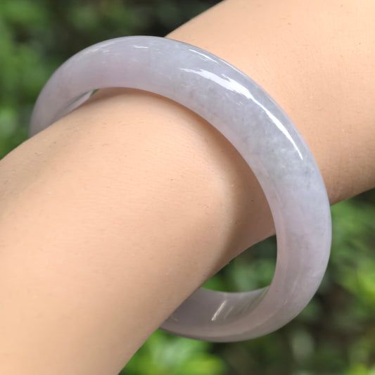 Angled wrist view of a pale lavender oval jadeite bangle, showing its softly mottled texture and glossy rounded exterior.