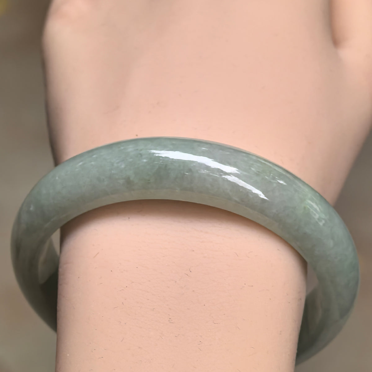 Front wrist view of a pale apple green jadeite bangle, highlighting its broad band, natural color variations and glossy polished surface.