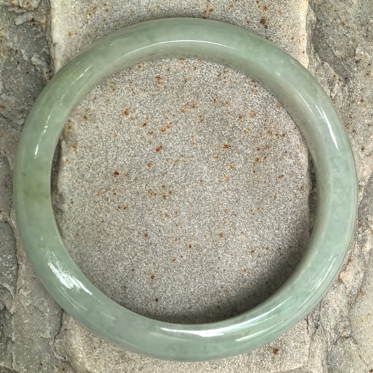 Overhead view of a pale apple green jadeite bangle on stone, showing its full circular shape and subtle variations in tone.