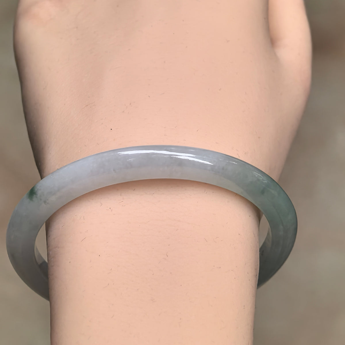 Front wrist view of a slim oval jadeite bangle, with a pale upper arc and a greener section along the right side.