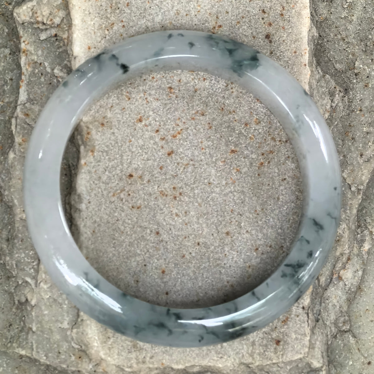 Overhead view of the jadeite D-shape bangle on stone, showing its full circular form and the distribution of deep green floating patterns.