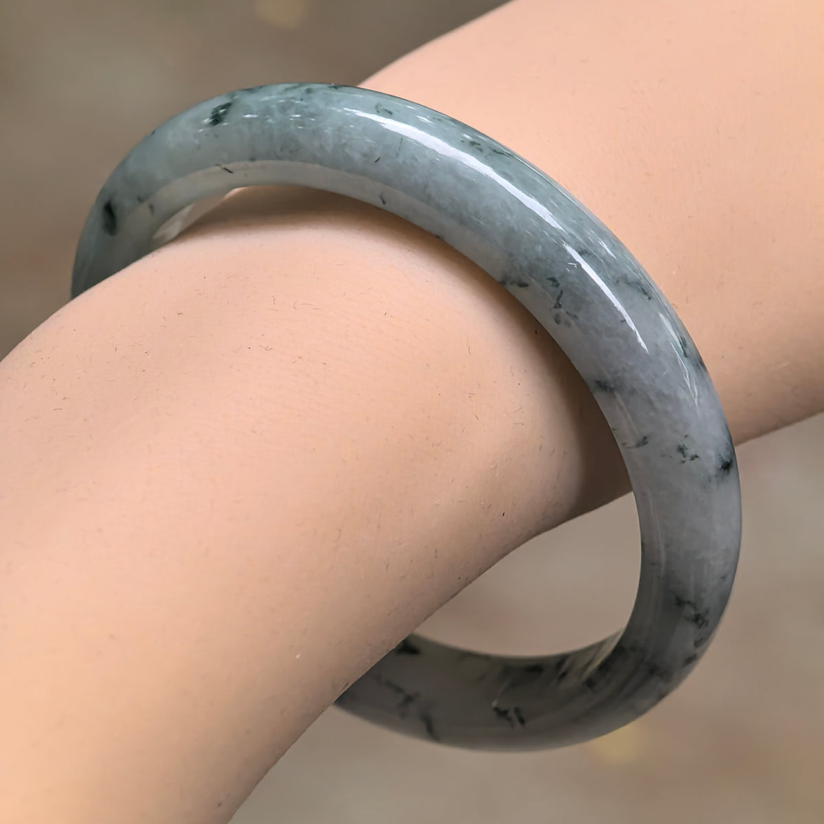 Angled wrist view of a fine glutinous jadeite slim D-shape bangle with delicate deep green floating patterns over a pale green base.