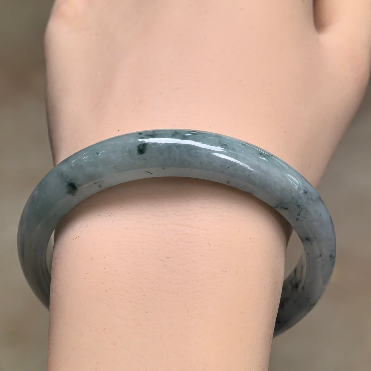 Front wrist view of the jadeite D-shape bangle, showing scattered deep green patterns and its smoothly polished outer surface.