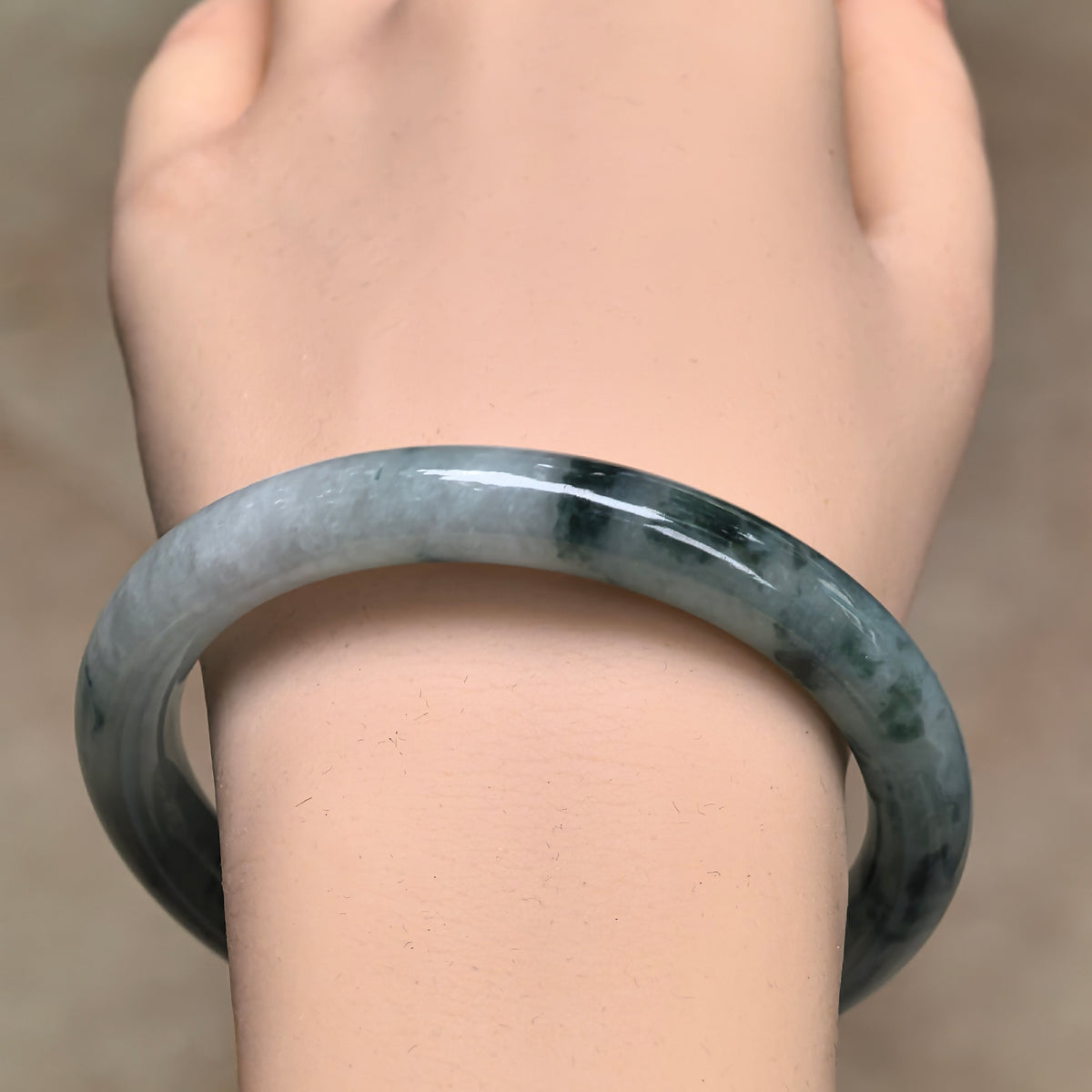 Front wrist view of the jadeite round-bar bangle, showing dark green floating patches and its smoothly polished curved surface.