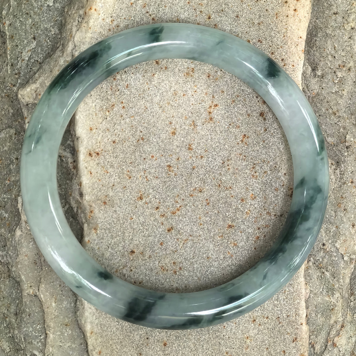 Overhead view of the jadeite bangle on textured stone, showing deep green floating patterns distributed around the full circle.