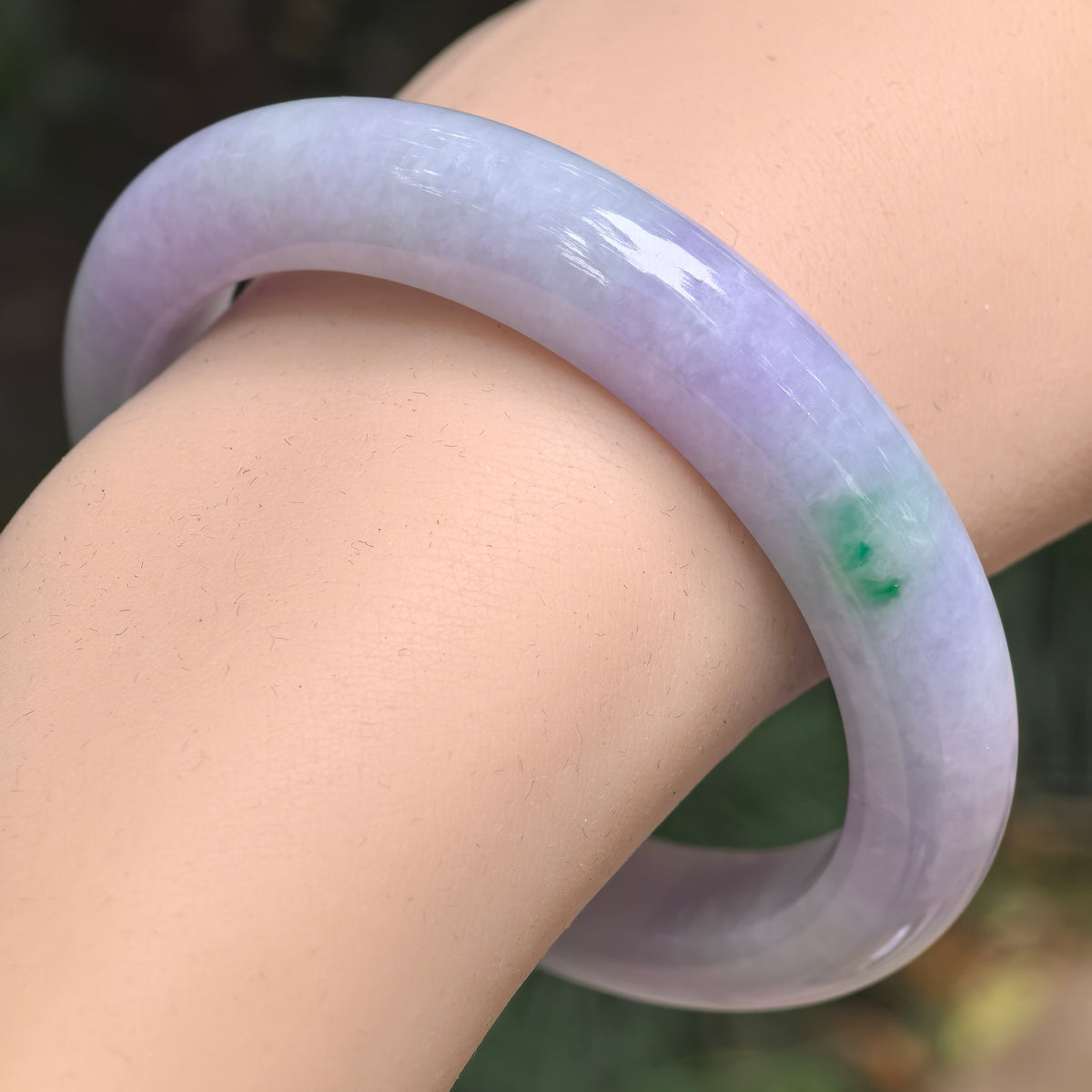 Angled wrist view of a glutinous pale lavender jadeite D-shape bangle with richer purple sections, whitish areas and a bright green accent on the right side.