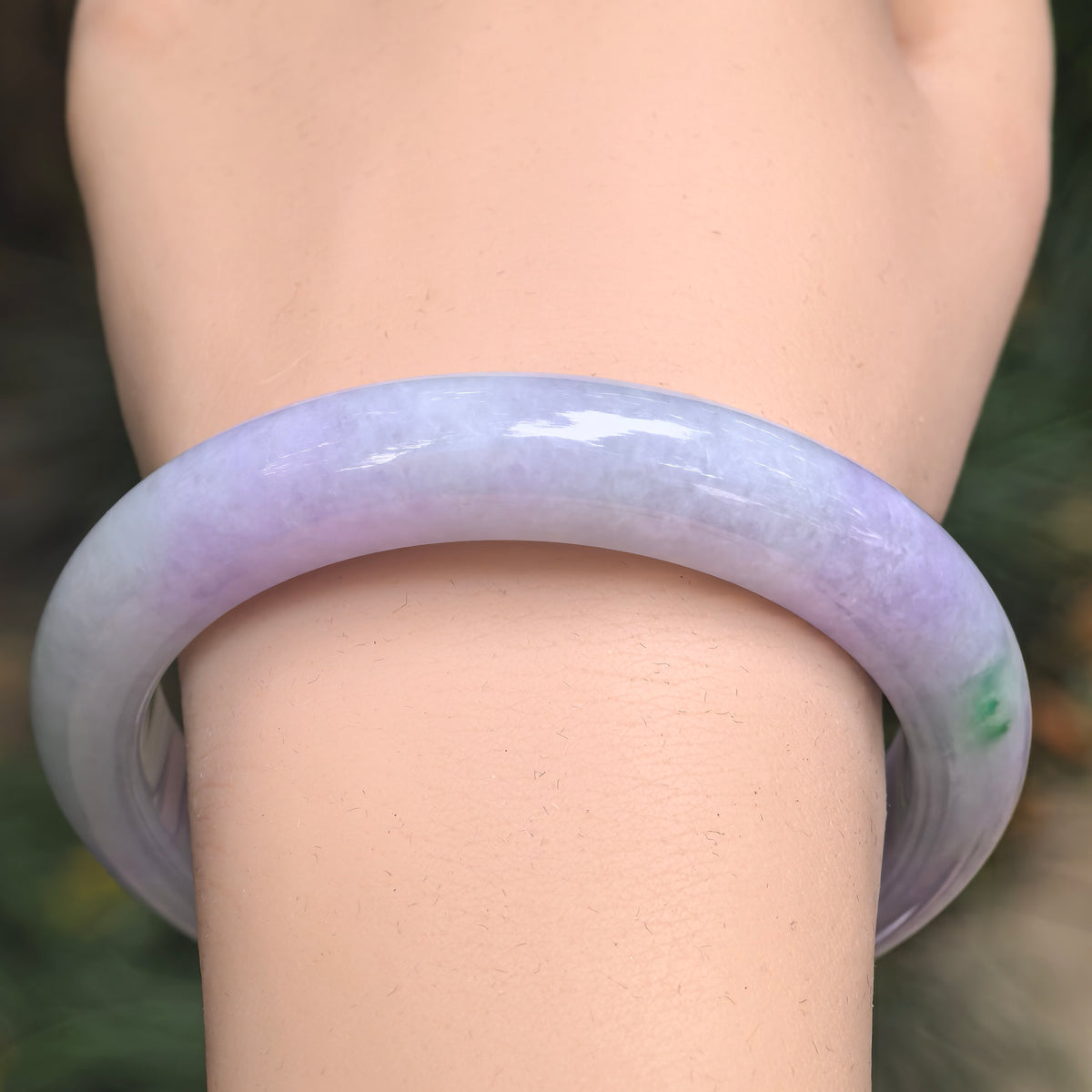 Front wrist view of a lavender jadeite D-shape bangle showing richer purple along the upper arc, a whitish section on the left and a small green accent on the right.