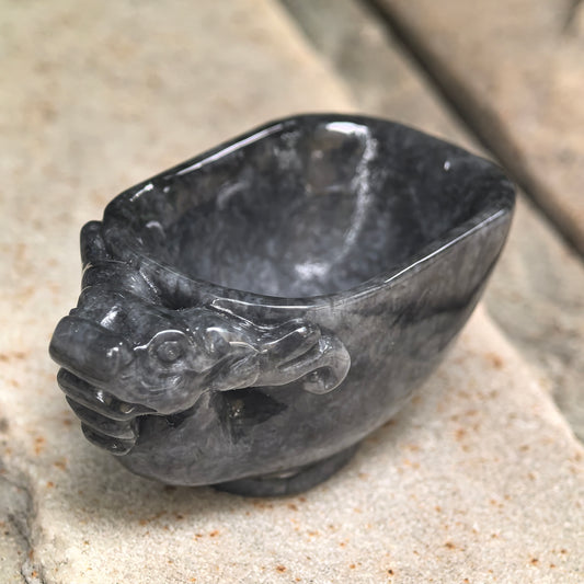 Three-quarter view of a black jadeite dragon-head cup on stone, showing the sculpted head, polished rim and hollowed interior.