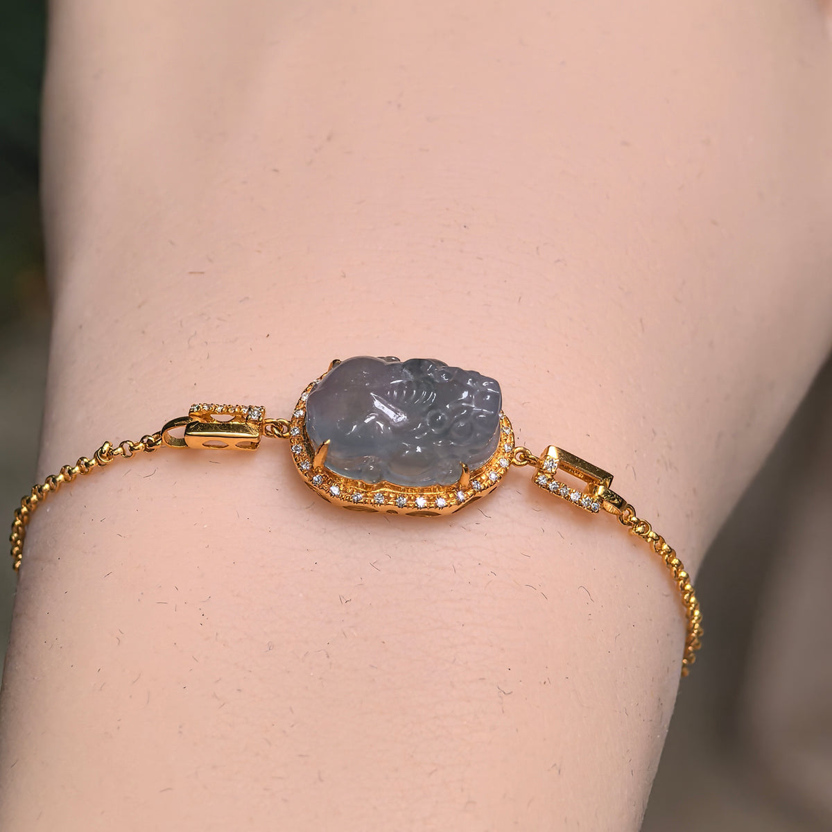Top view of a grayish purple jadeite Pixiu bracelet on textured stone, showing the carved centerpiece, diamond border and rectangular gold side links.