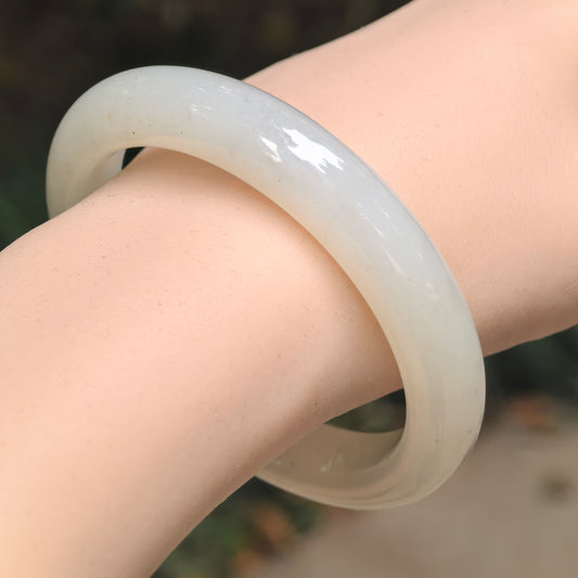 Angled wrist view of a white Hetian nephrite D-shape bangle, showing its polished surface and a few tiny black specks.