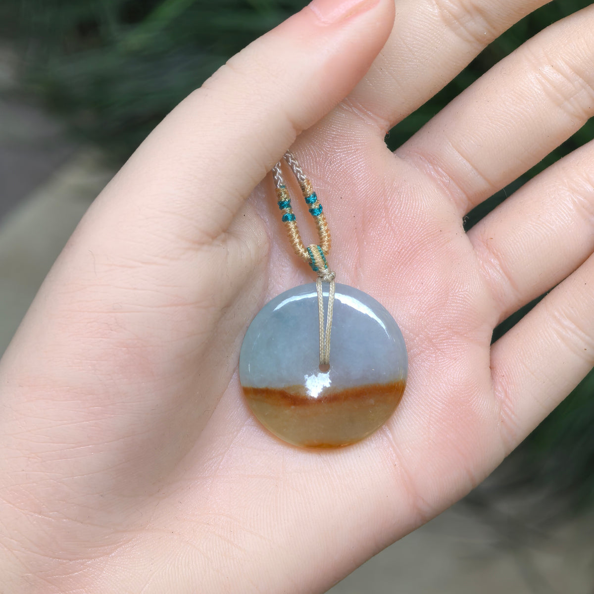 White and yellow jadeite Peace Pendant resting in a palm, showing its circular outline, small central opening and distinct natural color division.