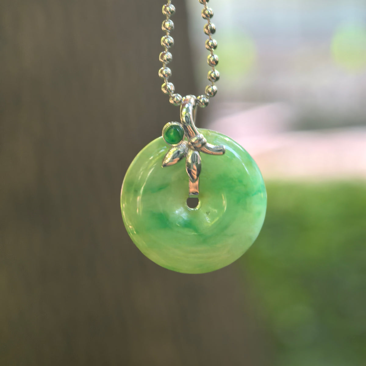 Icy glutinous green jadeite Peace Pendant hanging from a bead-style chain, showing floating green patterns and an 18K gold setting with leaf-like details.
