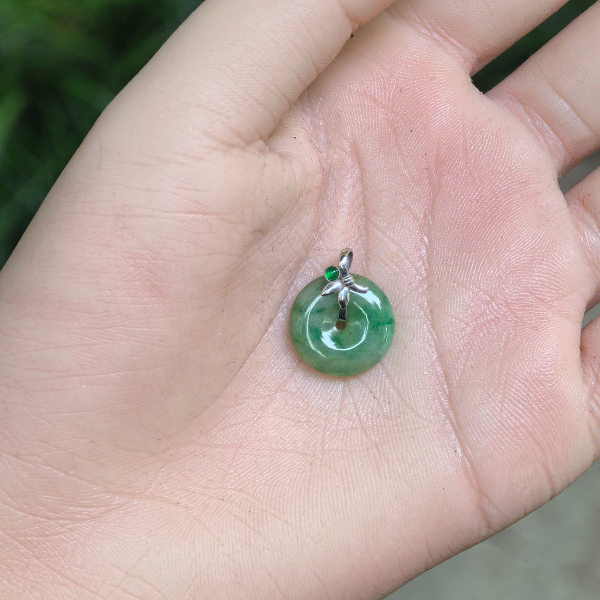 Small green jadeite Peace Pendant resting in a palm, showing its petite circular shape, central opening and decorative 18K gold setting.