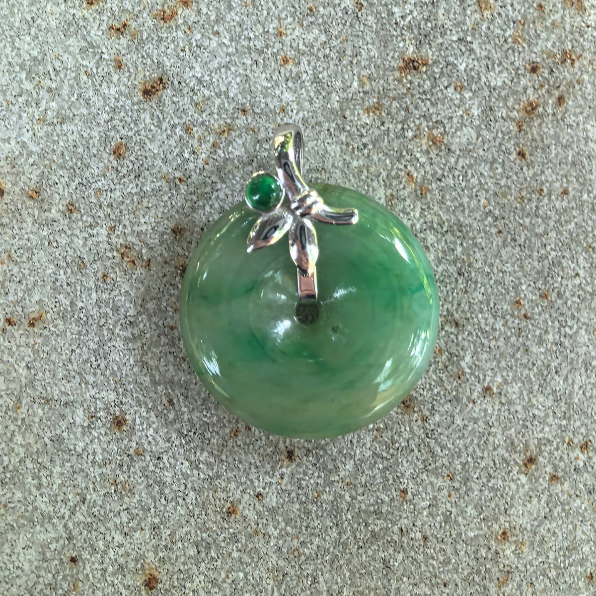 Front close-up of the green jadeite Peace Pendant on stone, showing the central opening and leaf-like details of the 18K gold setting.