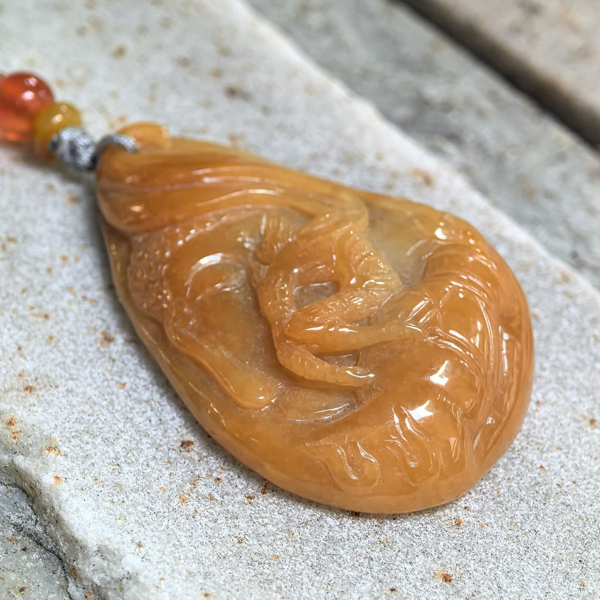 Angled close-up of the yellow jadeite Monkey King pendant on stone, highlighting the raised carving, curved motifs and polished surface.