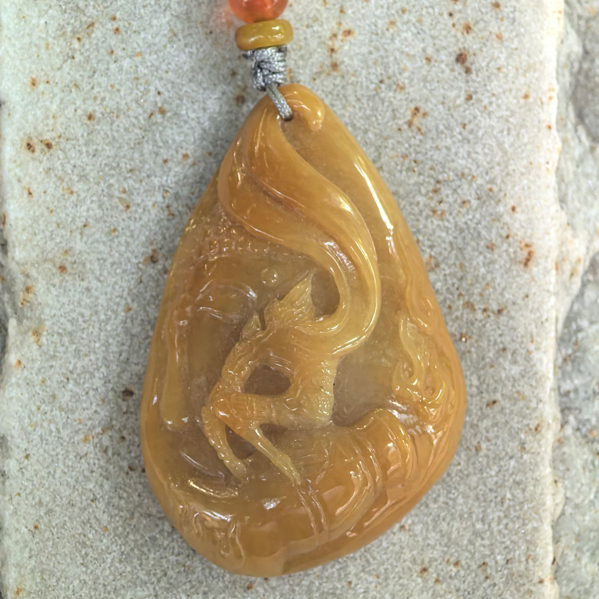 Front view of the yellow jadeite Monkey King pendant on textured stone, showing the carved figure, staff and sweeping curved details.