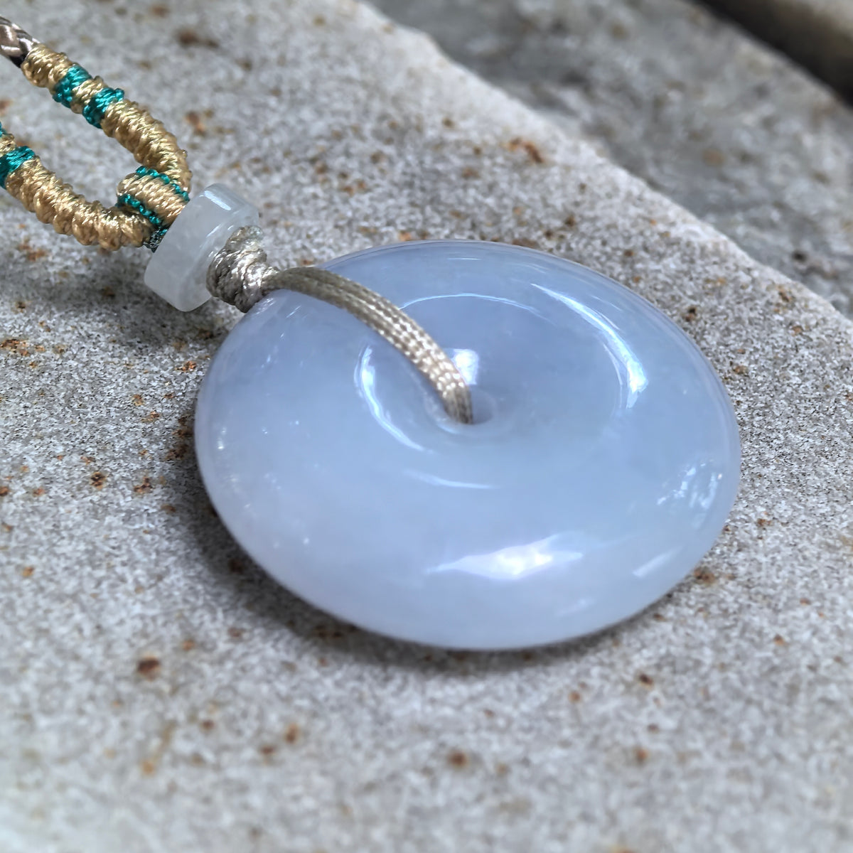 Angled close-up of the blue-lavender jadeite Peace Pendant on stone, showing its rounded profile, polished surface, and central opening.