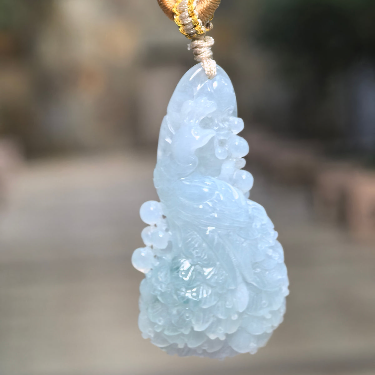 Blue icy glutinous jadeite Phoenix Pendant hanging from a knotted cord, showing an elongated freeform outline and layered tail feathers.