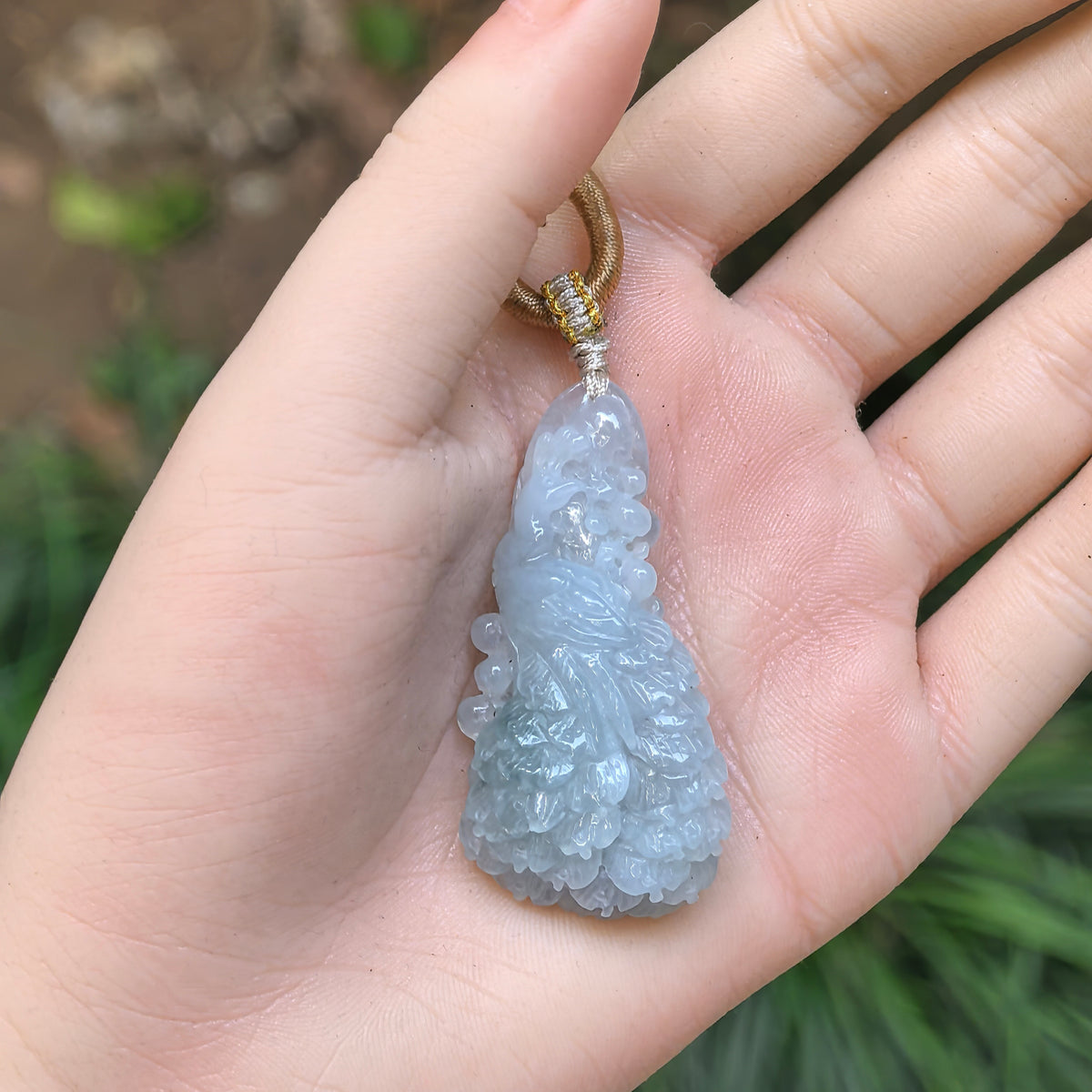 Blue jadeite Phoenix Pendant resting on a palm, showing its carved bird motif, rounded scrolls and decorative cord knots.
