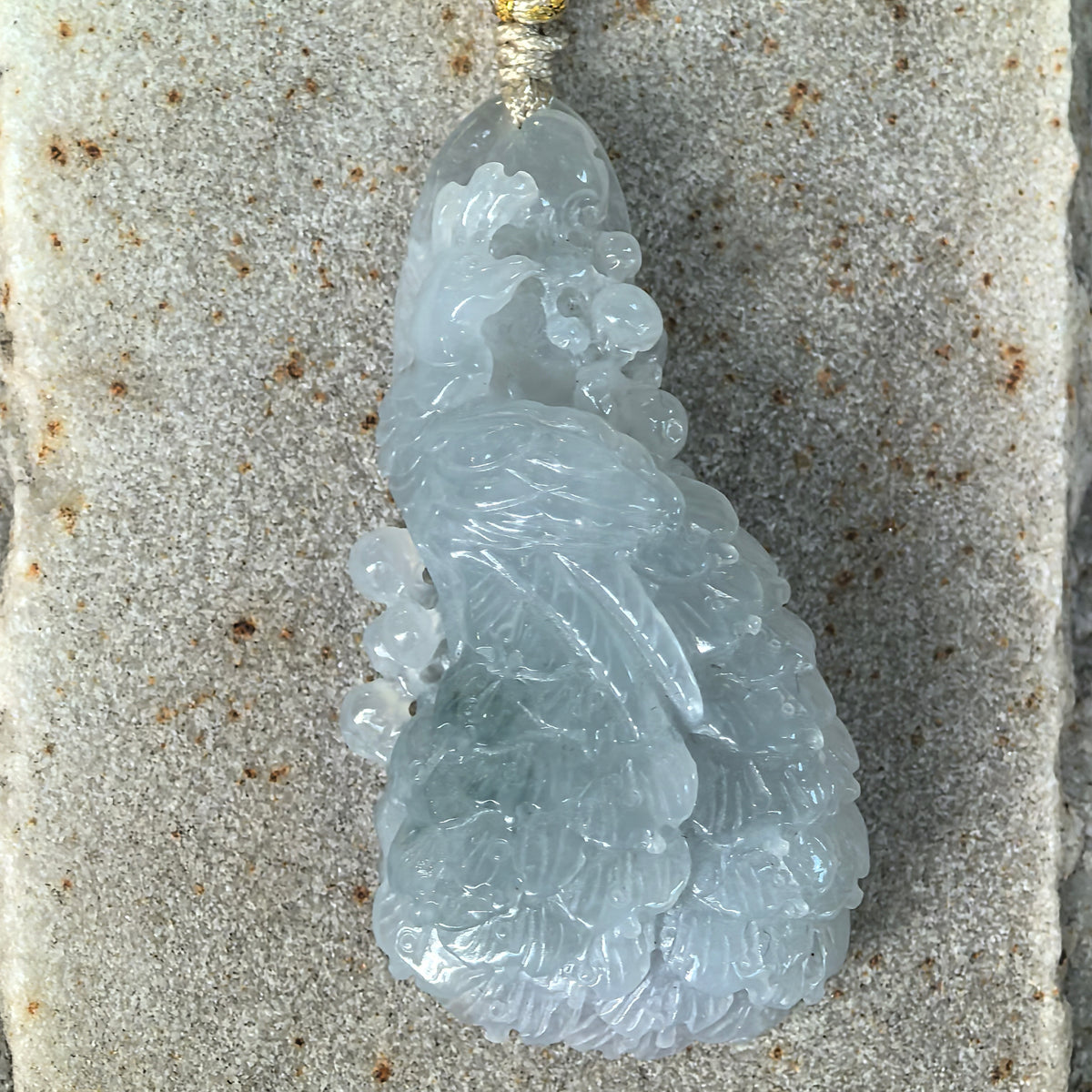 Front close-up of a blue jadeite Phoenix Pendant on stone, showing the curved neck, detailed wing and layered feather carving.