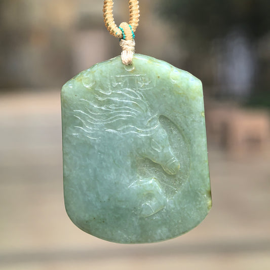 Muted gray-green glutinous jadeite Horse Plaque Pendant hanging from a beige knotted cord, showing a horse head in profile with a flowing mane.