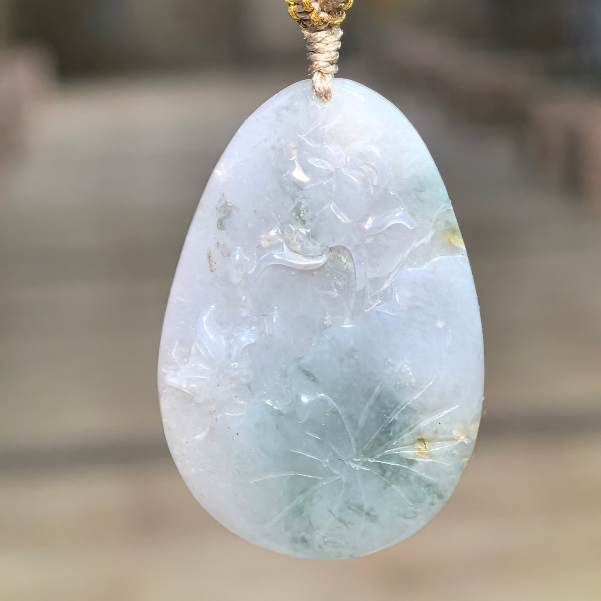 Blue glutinous jadeite Floral Plaque Pendant hanging from a knotted cord, showing flower and leaf relief carving with deeper color accents near the bottom.