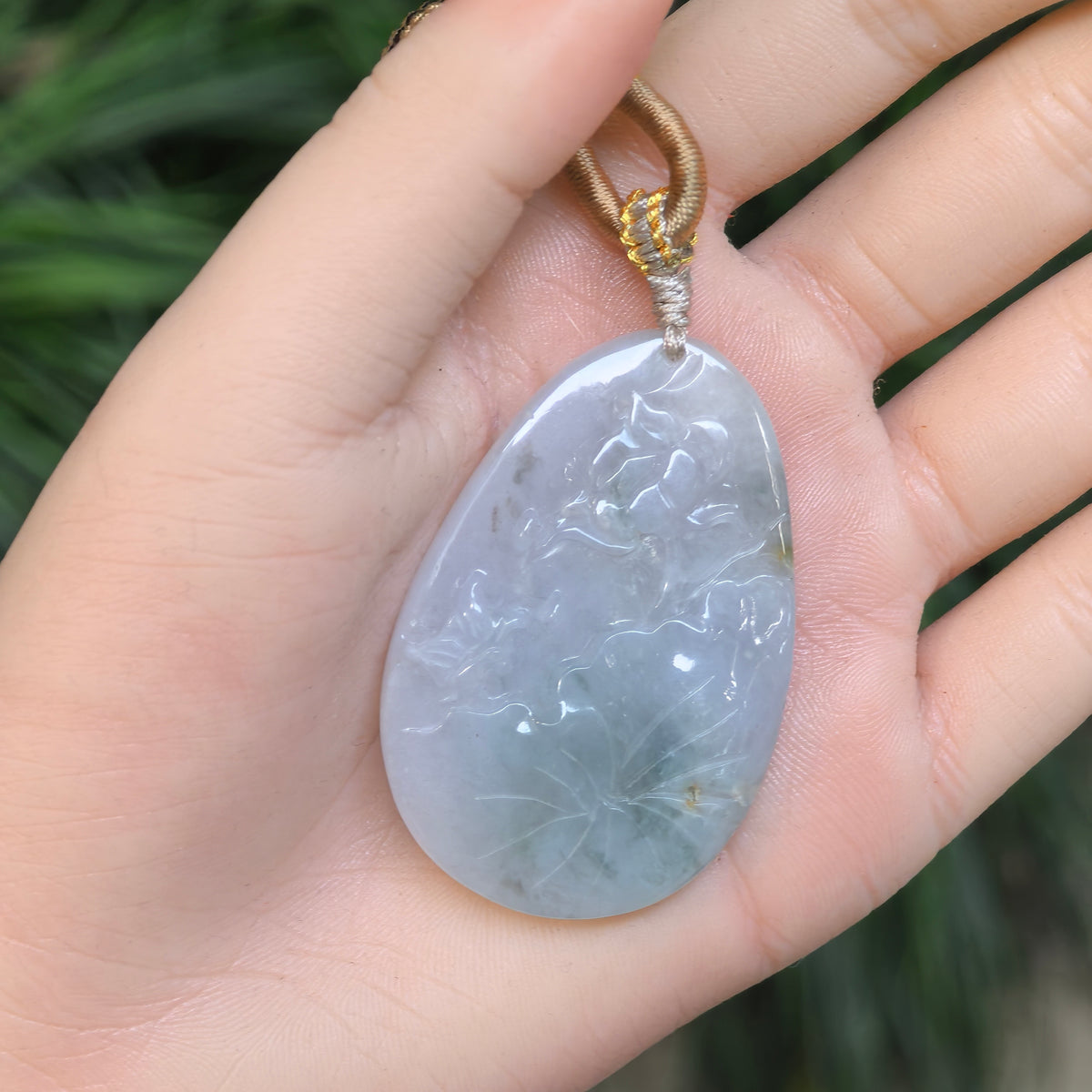 Blue jadeite Floral Plaque Pendant resting on a palm, showing its tapered outline, rounded lower edge and decorative cord knots.