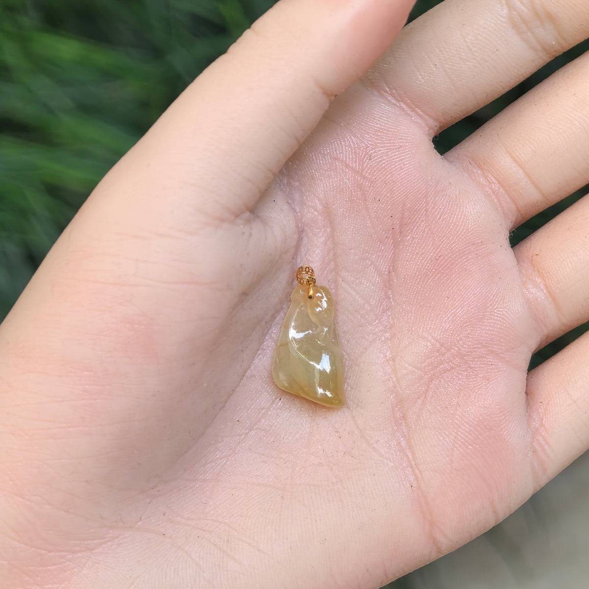 Small yellow jadeite Horse Head Pendant resting on a palm, showing its asymmetric outline, polished carving and 18K gold bail.