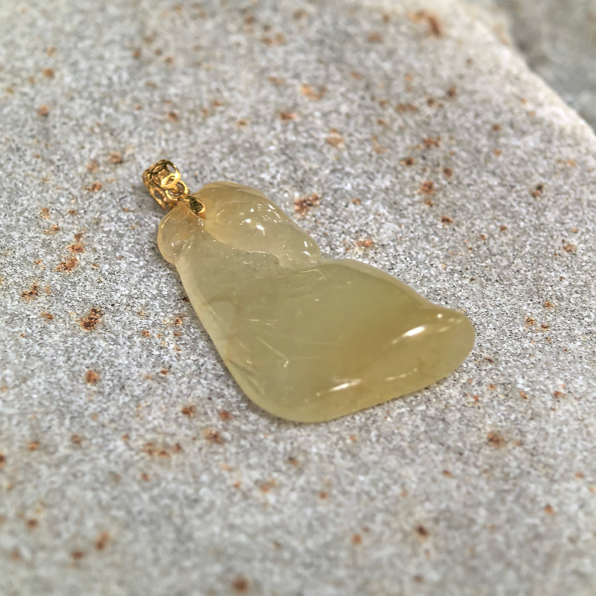 Angled close-up of the yellow jadeite Horse Head Pendant on a stone surface, highlighting its curved carving and patterned gold bail.