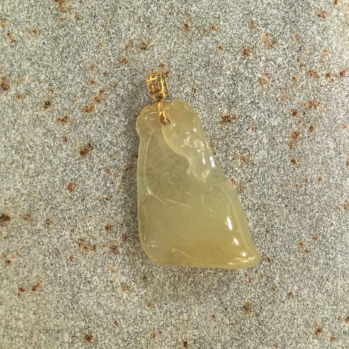 Front view of the yellow jadeite Horse Head Pendant on a stone surface, showing its stylized profile and smooth, polished contours.