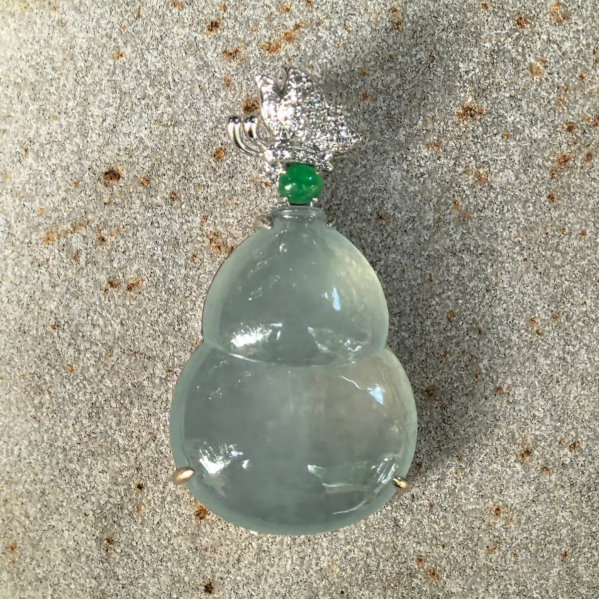 Front close-up of the icy light green jadeite Gourd Pendant on a stone surface, showing its polished lobes, green accent stone and diamond butterfly detail.