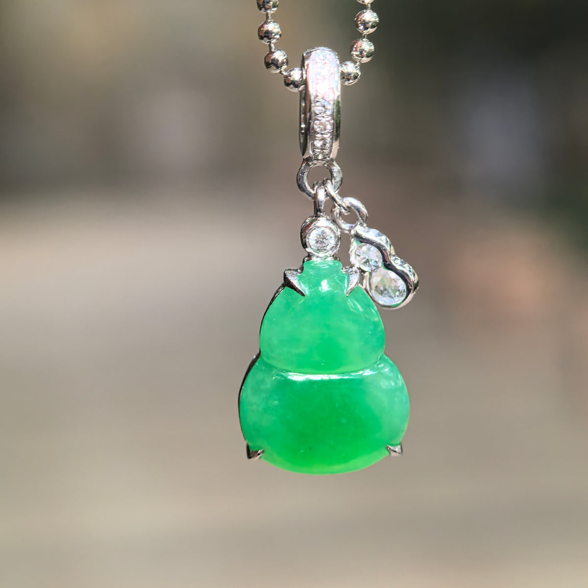 Icy vivid green jadeite Gourd Pendant hanging from a bead-style chain, showing its 18K gold setting, diamond-accented bail and small diamond-set Gourd charm.
