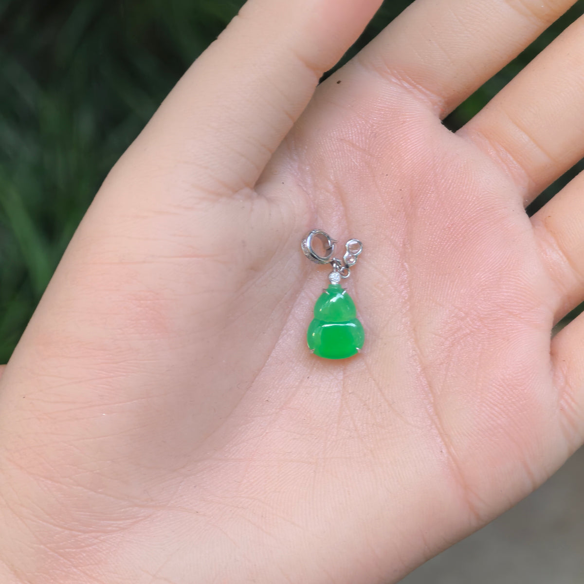 Small vivid green jadeite Gourd Pendant resting in a palm, showing its petite proportions, rounded lobes and 18K gold setting.