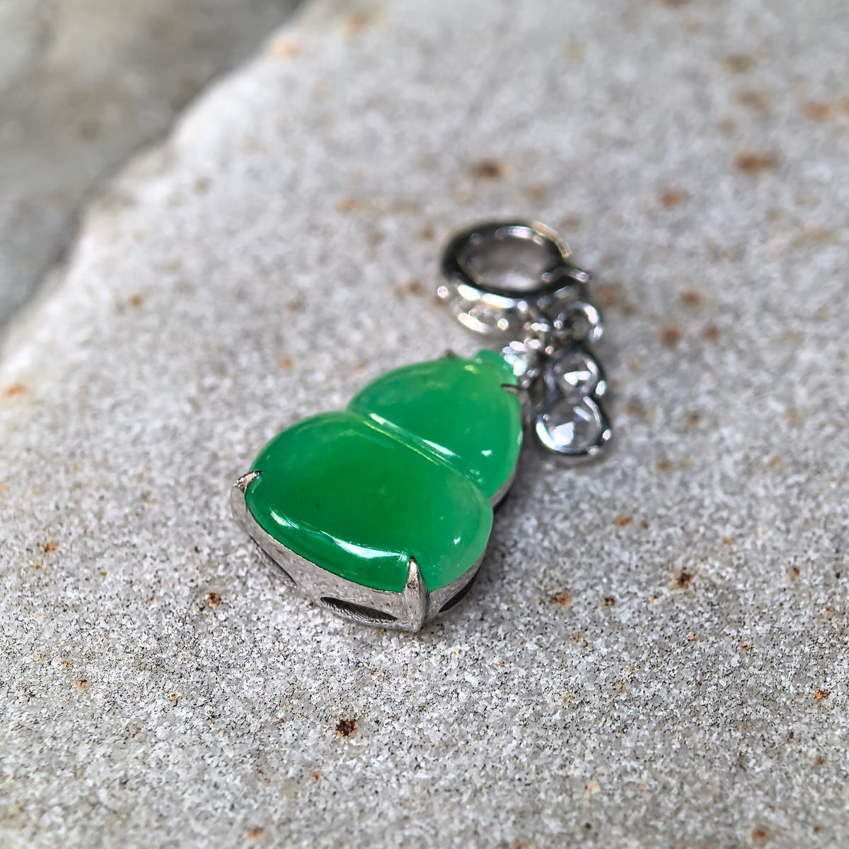 Angled close-up of the green jadeite Gourd Pendant on stone, highlighting the rounded surface, 18K gold prongs and side of the setting.