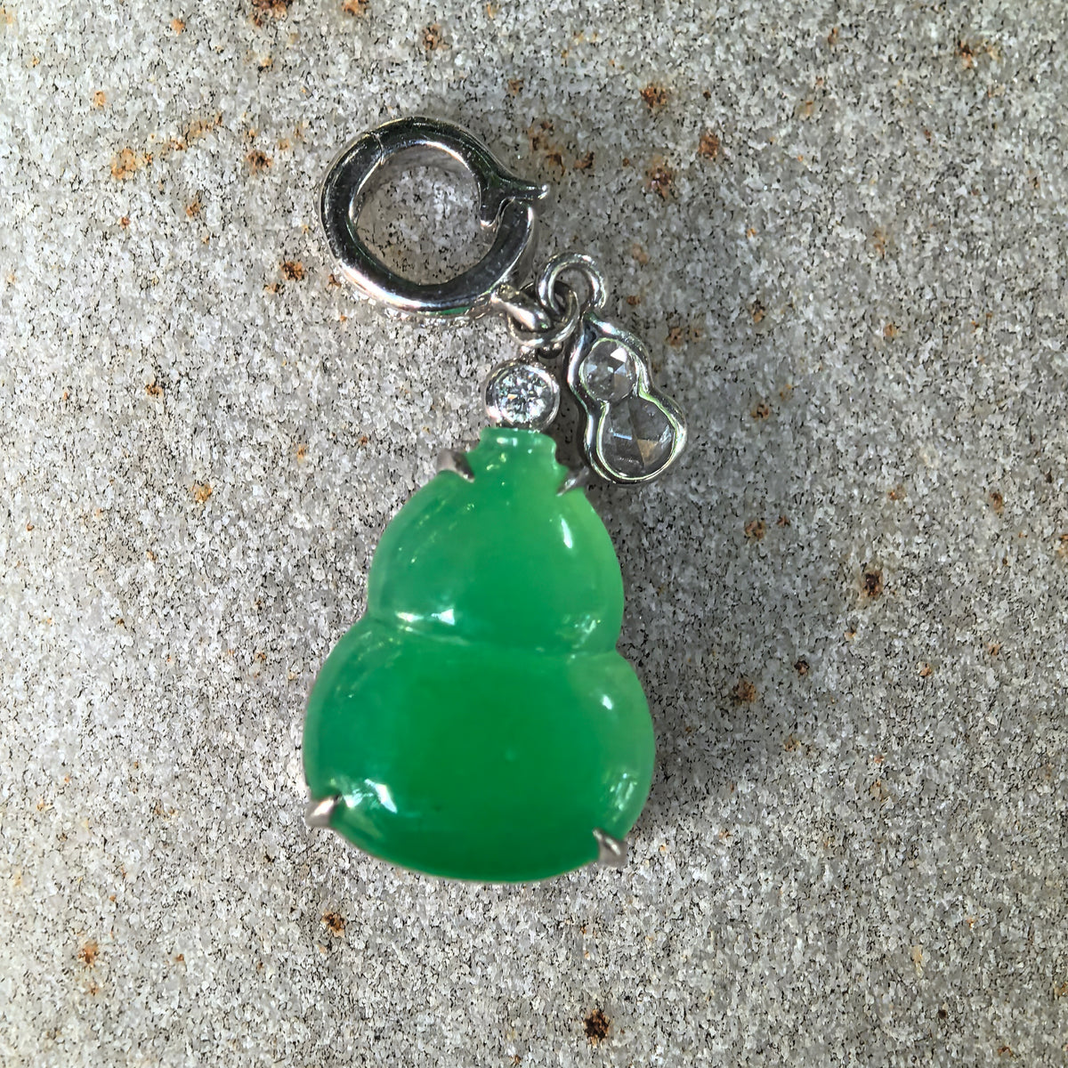 Front close-up of the vivid green jadeite Gourd Pendant on textured stone, showing the polished surface and small diamond-set Gourd charm beside it.