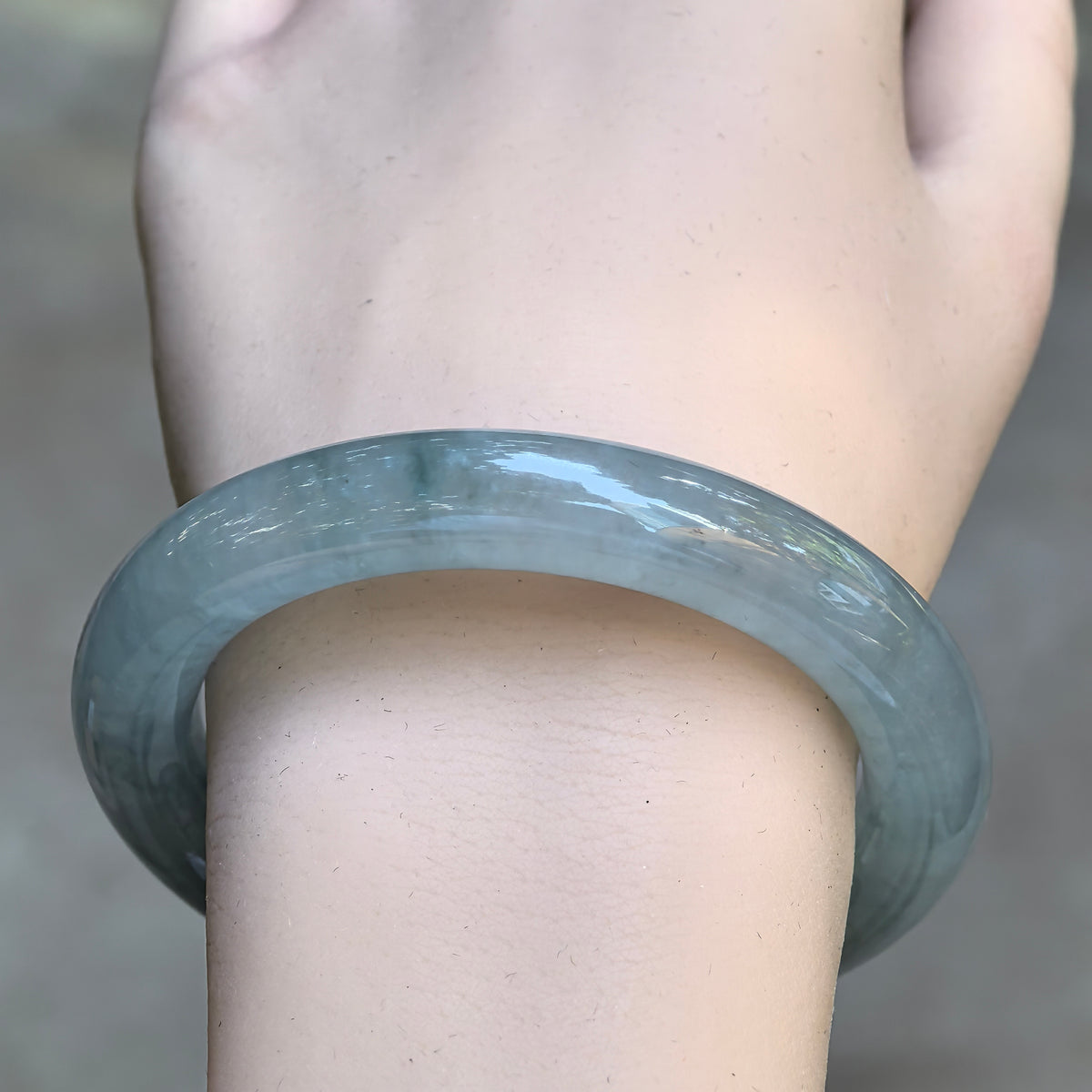 Front view of the light green round-bar jadeite bangle on the wrist, showing its translucent texture, natural tonal variations, and smooth luster.