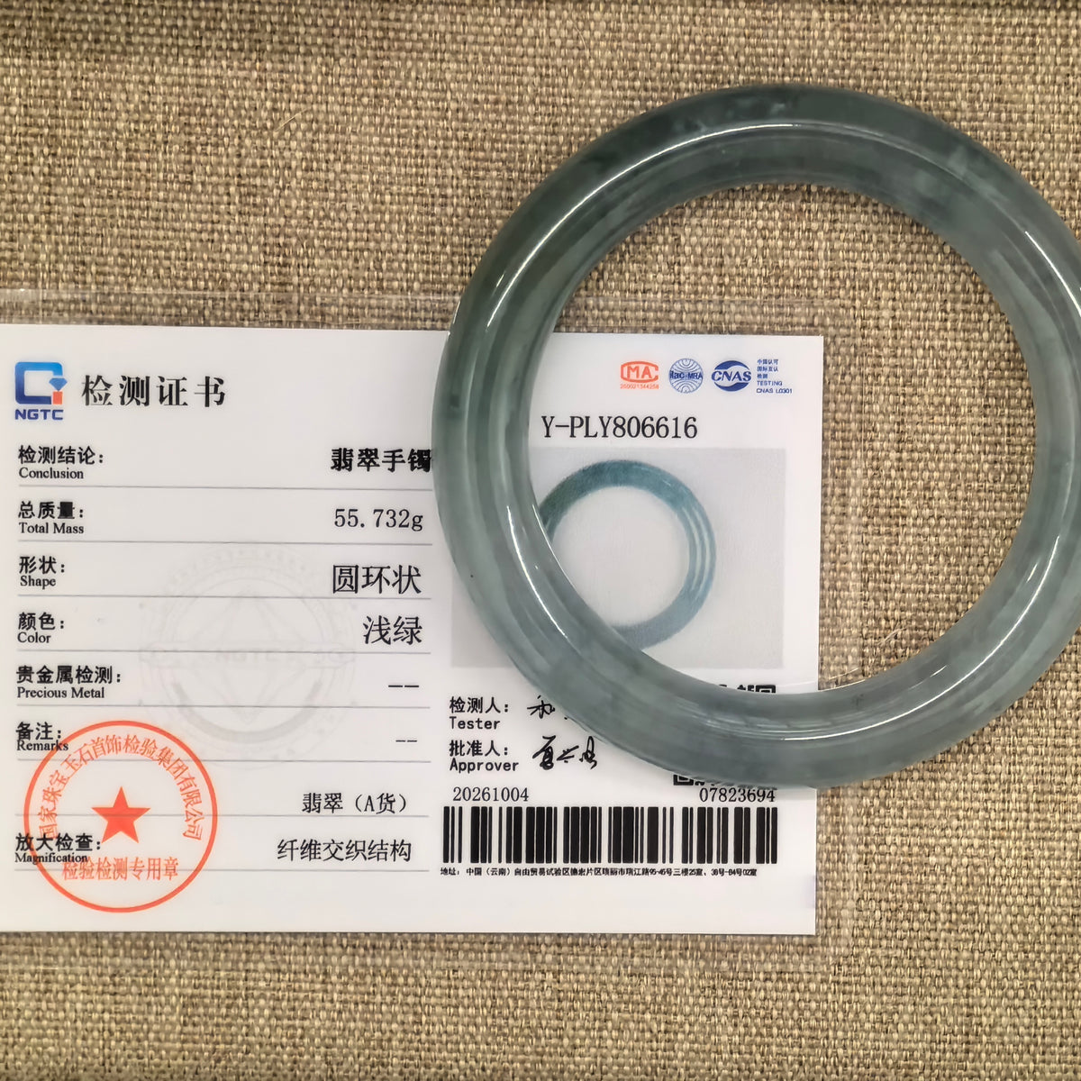 Light green round-bar jadeite bangle displayed with its matching NGTC certificate numbered Y-PLY806616 on a woven background.