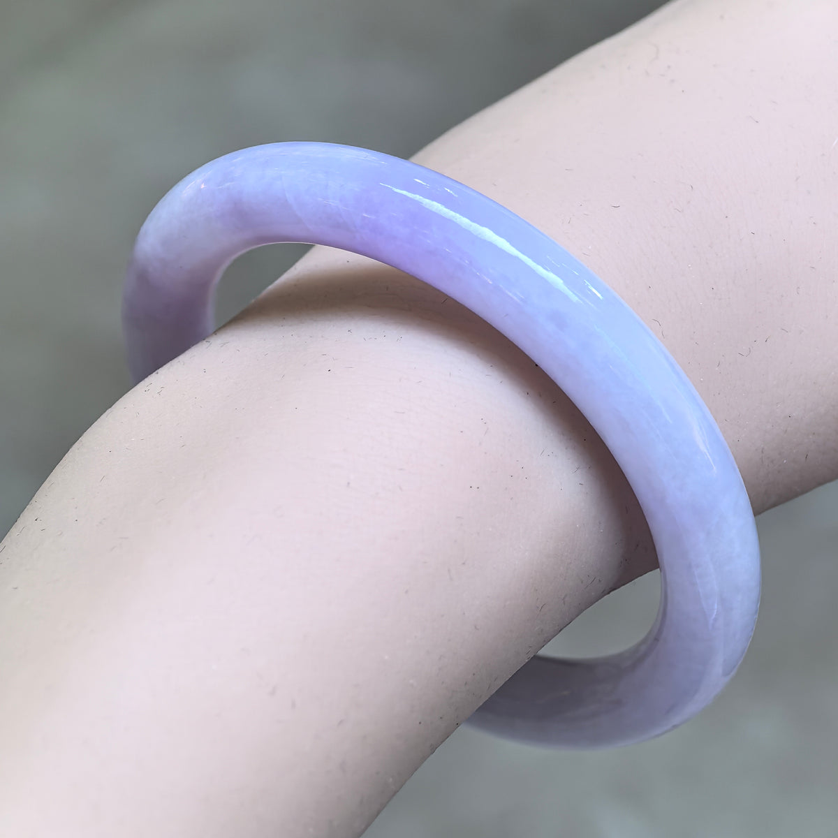 Angled wrist view of a glutinous lavender round-bar jadeite bangle showing its rounded profile and polished finish.