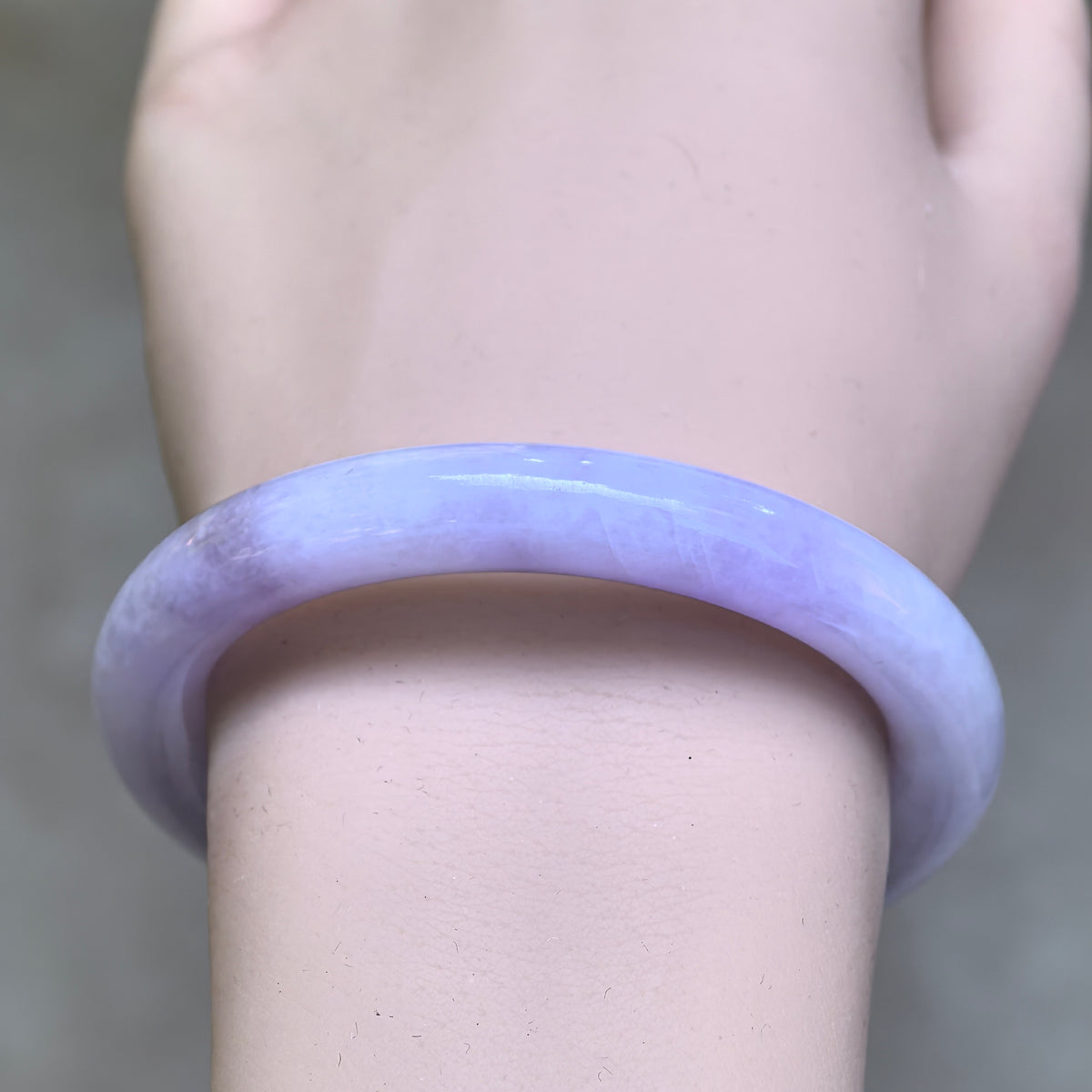 Front wrist view of a lavender round-bar jadeite bangle showing natural tonal variations and cotton-like streaks.