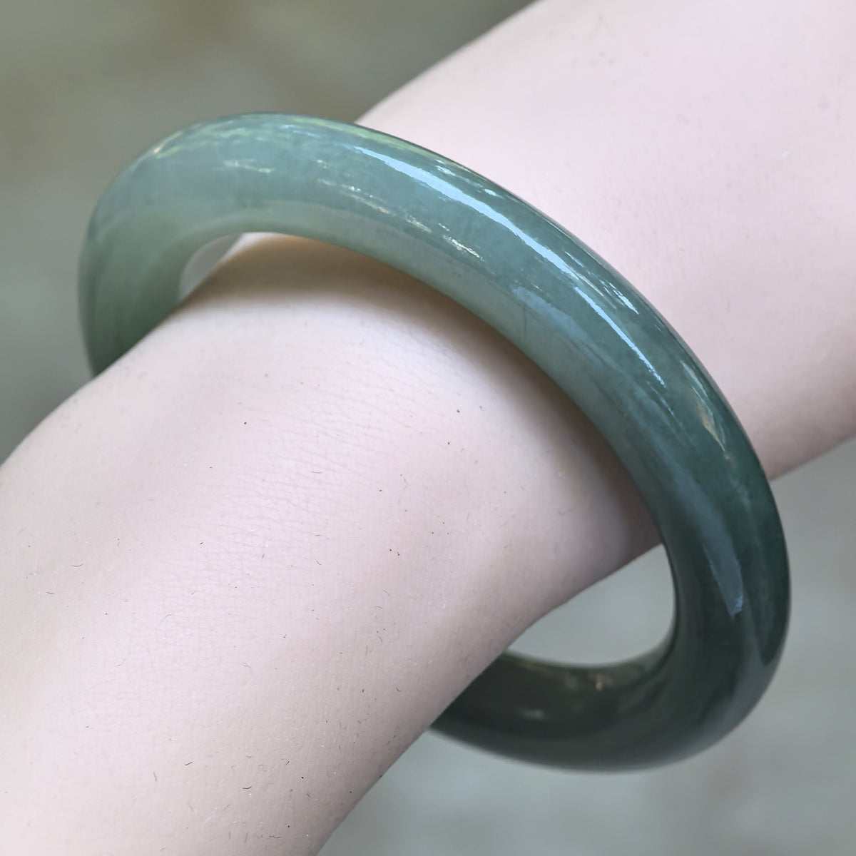 Angled close-up of a green round-bar jadeite bangle worn on the wrist, showing its rounded profile and polished surface.