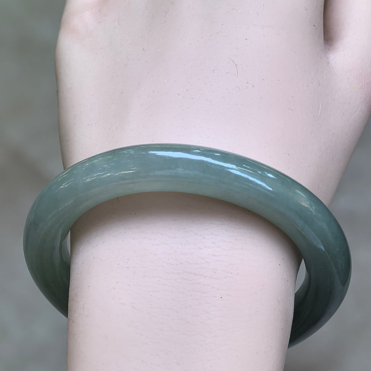 Front view of the green round-bar jadeite bangle on the wrist, showing its muted color, fine texture, and natural tonal variations.