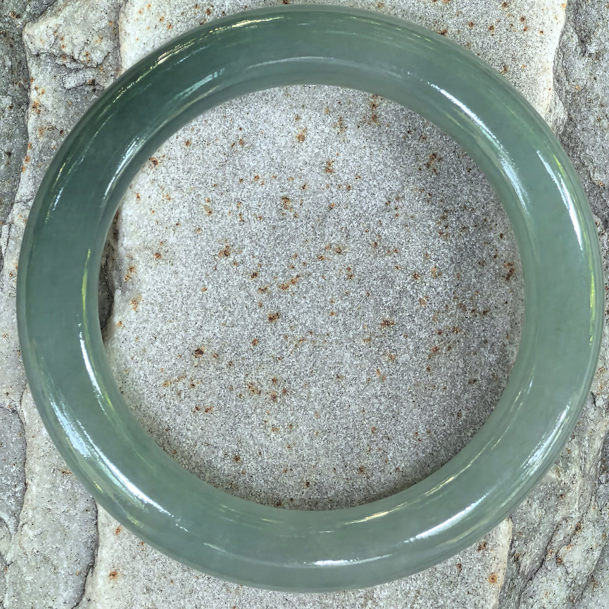 Overhead view of the green round-bar jadeite bangle on stone, showing its circular outline and softly translucent texture.