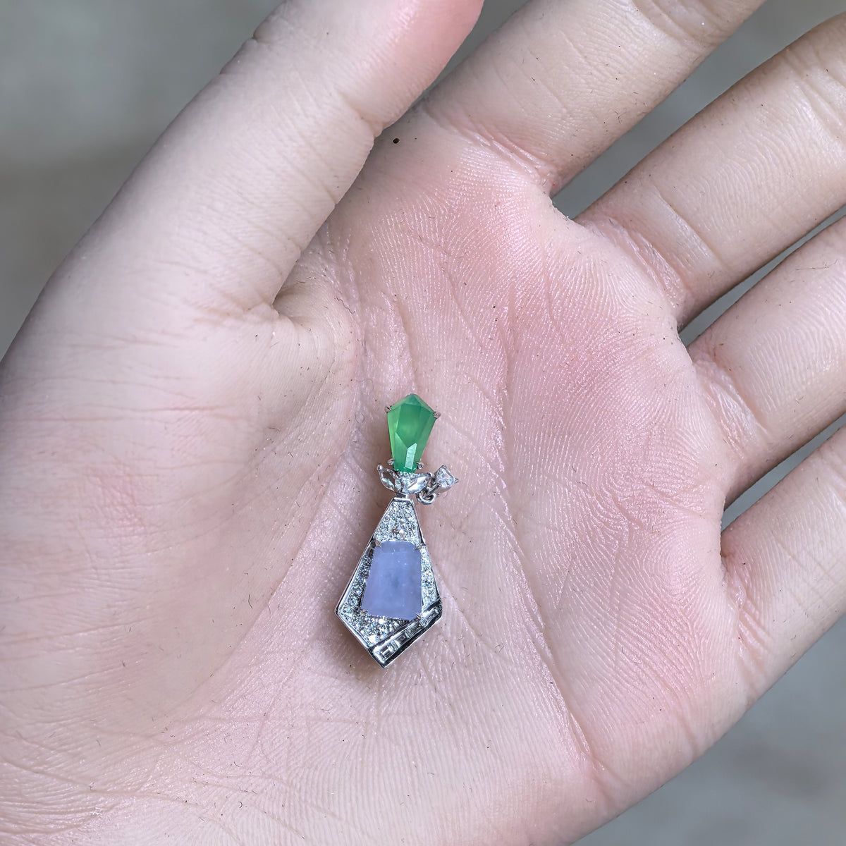 Lavender and green jadeite geometric kite-shaped pendant resting in a palm, showing its overall silhouette and angular diamond frame.