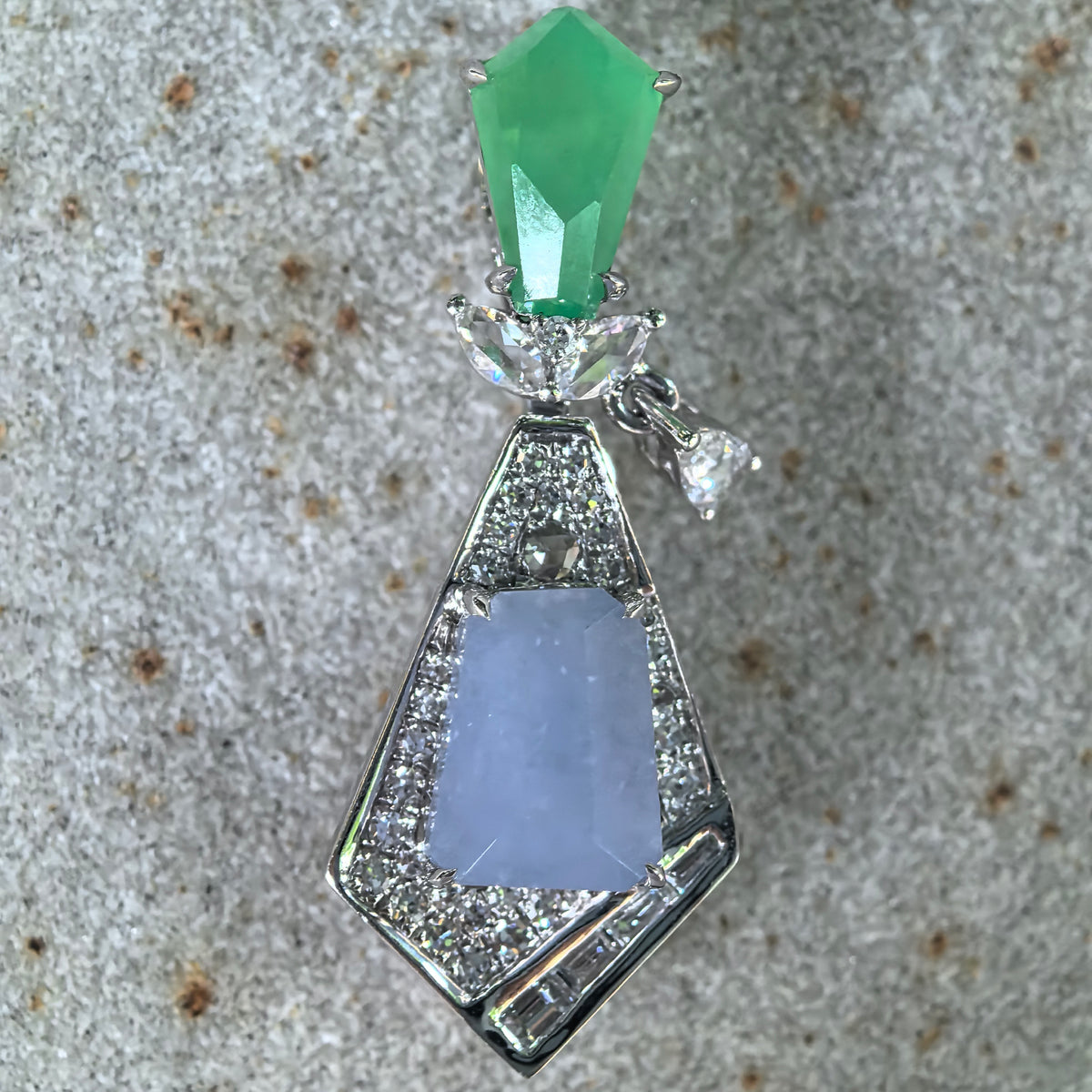 Front close-up of an icy lavender and green jadeite geometric kite-shaped pendant on stone, showing the polished jadeite surfaces and diamond accents.