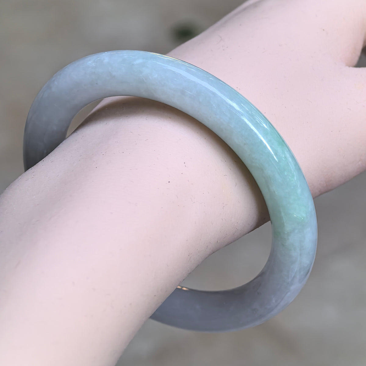 Angled wrist view of a glutinous jadeite round-bar bangle, showing pale lavender and pale green sections along the rounded profile.