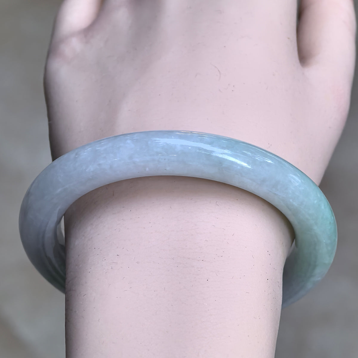 Front wrist view of a pale green and pale lavender round-bar jadeite bangle, showing its soft color transition and polished surface.