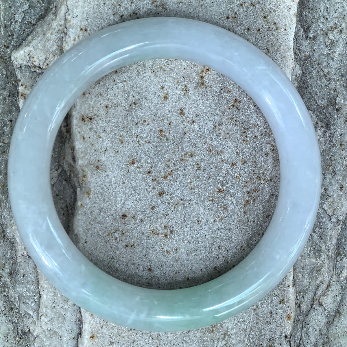 Overhead view of a glutinous jadeite round-bar bangle on stone, showing the pale green and pale lavender color distribution.