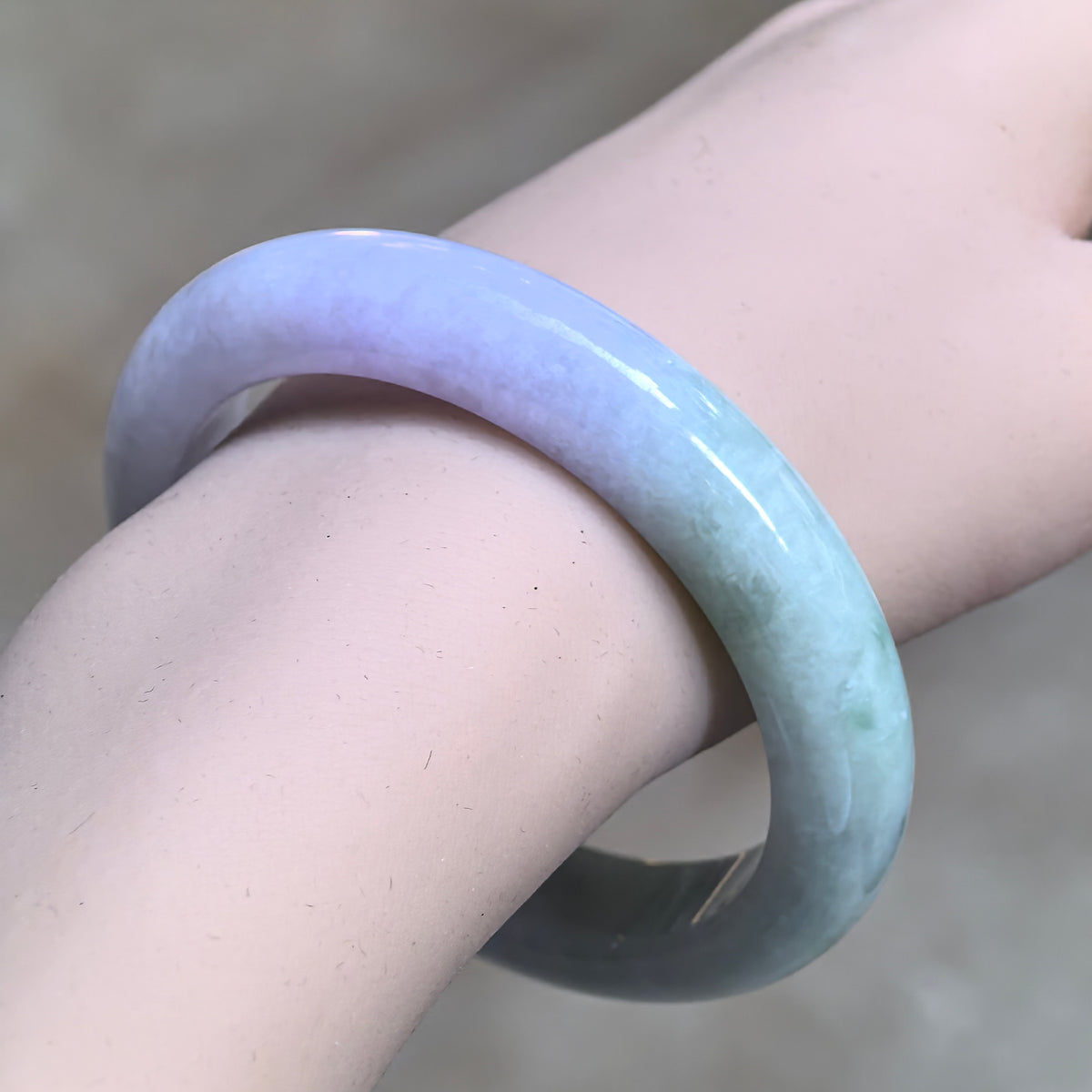 Angled wrist view of a glutinous jadeite D-shape bangle, showing the transition from pale lavender to pale green.